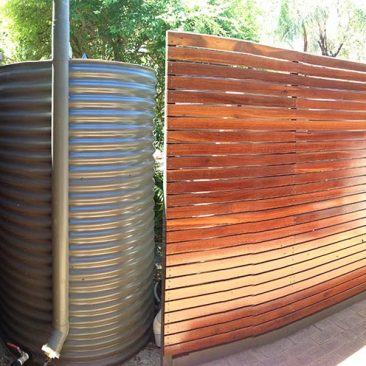 slimline rainwater tank oval shape with wooden fence to hide it