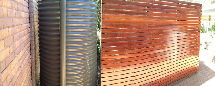 slimline rainwater tank oval shape with wooden fence to hide it