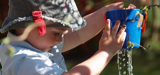 Child holding a water can with holes and water dripping through