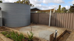 Galvanised rainwater tank on pad near brown fence in Greenock SA